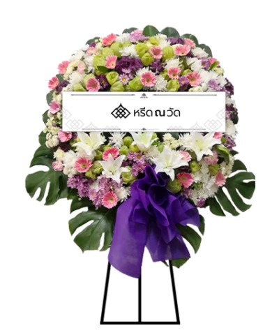 พวงหรีดดอกไม้สด ตกแต่งด้วยดอกเบญจมาศ ดอกเยอบีร่า ดอกคาร์เนชัน ดอกลิลลี่ และสวอนแพลนท์ พร้อมโบว์สีม่วงขนาดใหญ่