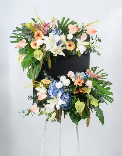 รายละเอียดมุมบนของพวงหรีดดอกไม้สดแบบตั้งพื้น พร้อมหน้าวัวสีพีชและลิลลี่สีขาว
