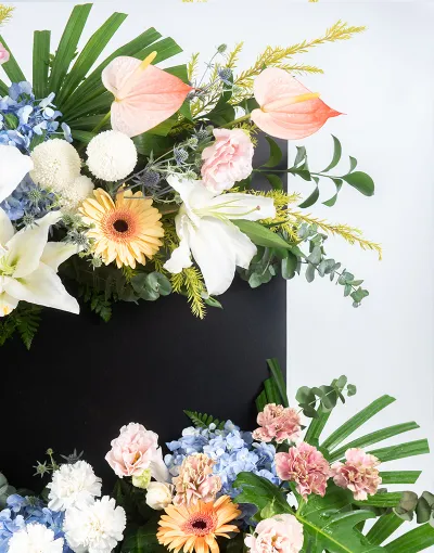 รายละเอียดมุมล่างของพวงหรีดดอกไม้สดแบบตั้งพื้น พร้อมไฮเดรนเยียสีฟ้าและใบมอนสเตอร่า