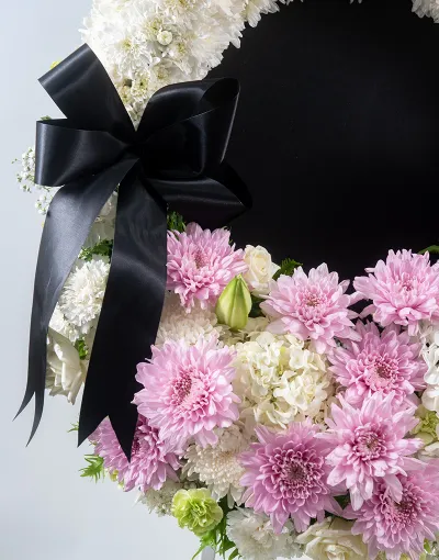 รายละเอียดดอกไม้โทนชมพูขาวและโบว์สีดำบนพวงหรีด